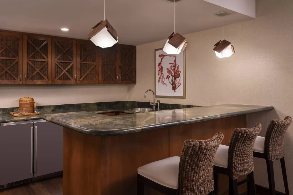 Bar with dark granite, wicker stools, wood cabinets, and geometric pendant lights.