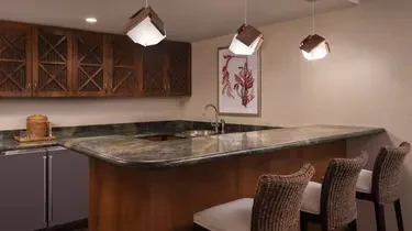 Contemporary bar with curved granite counter, rattan stools, and pendant lights.