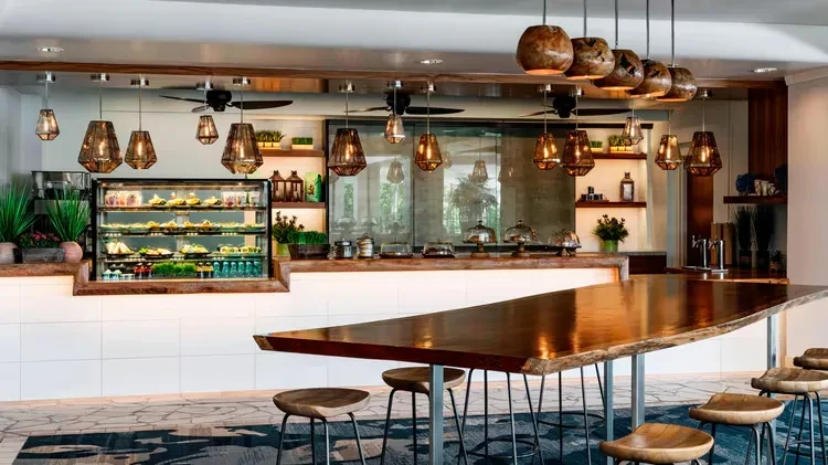 Modern restaurant interior with food display, communal table, and warm lighting.