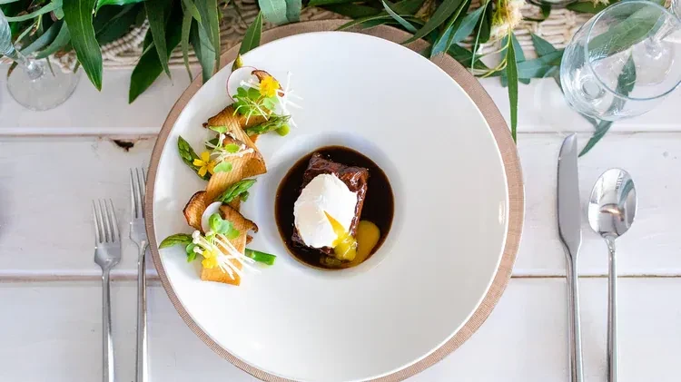 Top-down view of plated braised meat, poached egg, and colorful vegetables.