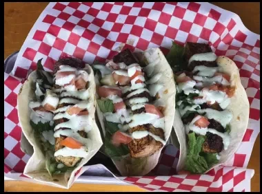 Three soft-shell tacos with protein, lettuce, tomatoes, drizzled green sauce.