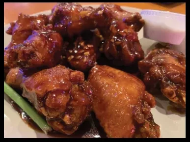 Plate of glossy dark chicken wings, sesame seeds, and dipping sauce.