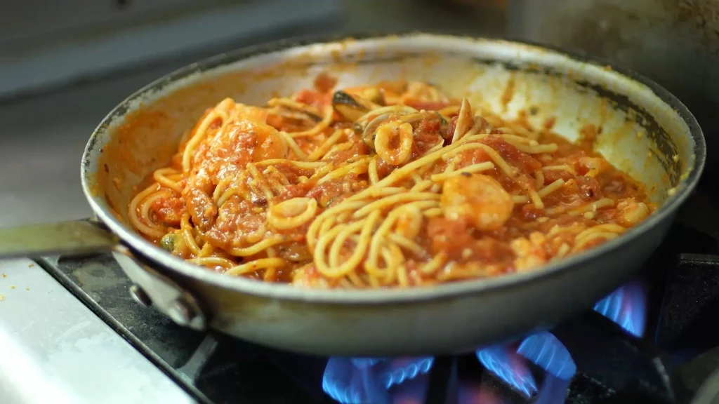 Pan of spaghetti with seafood and tomato sauce cooking on flames.