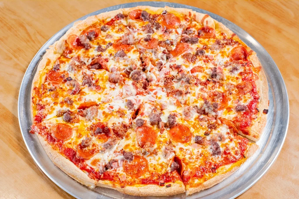 A sliced meat lover's pizza topped with pepperoni and sausage on a pan.