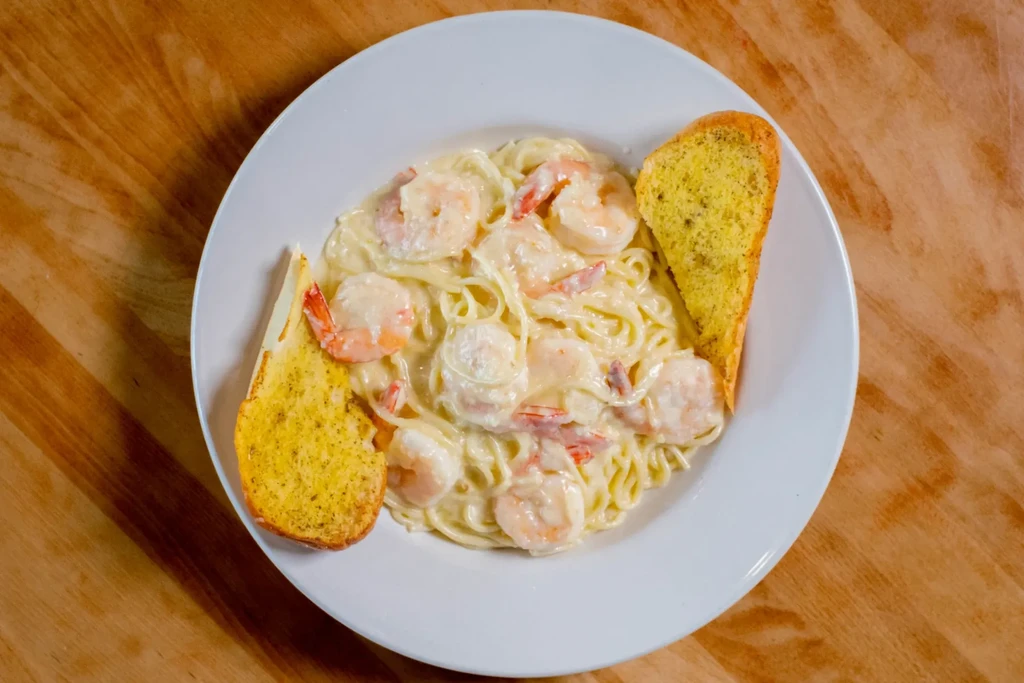 Creamy shrimp pasta with garlic bread on a wooden table.