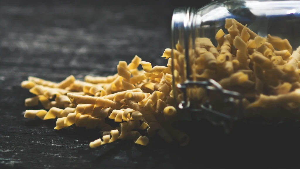 Uncooked twisted pasta spilled from an overturned jar on a dark table.