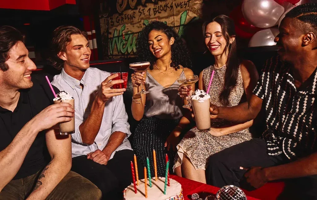 Five young adults celebrating a birthday with cake and colorful drinks.