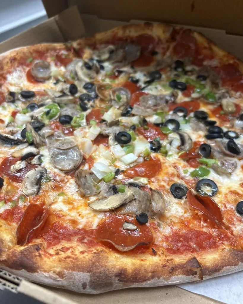 Freshly baked pizza with multiple toppings in a cardboard pizza box.