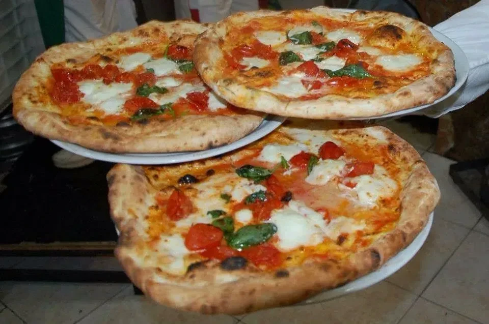 Hand presenting three stacked Margherita pizzas with bubbly crusts.