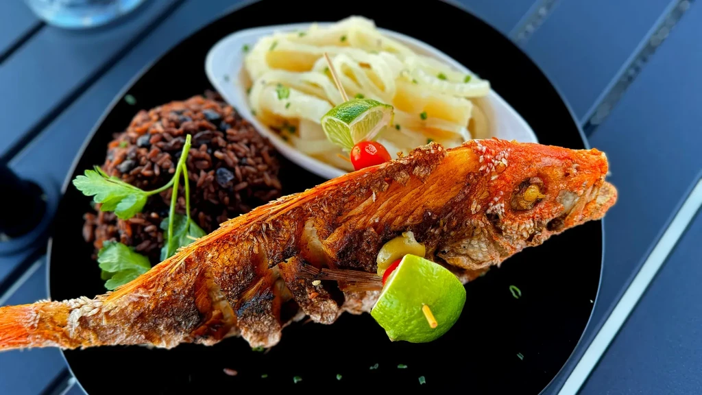Crispy fried fish, rice, black beans, and yuca on black plate.