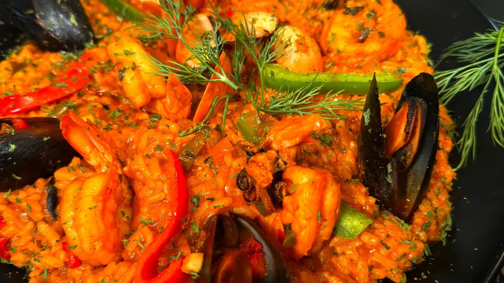 Vibrant orange-red seafood dish with shrimp, mussels, peppers, and dill.
