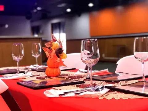 Set dining table with red tablecloth, pumpkin centerpiece, and autumn foliage.