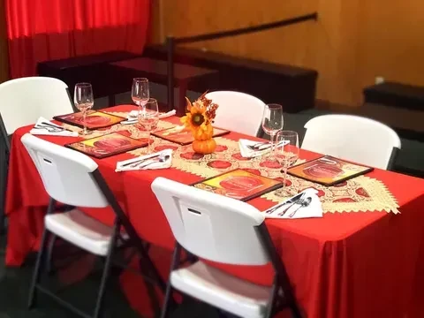 Dining table set with red cloth, autumn placemats, and pumpkin centerpiece.