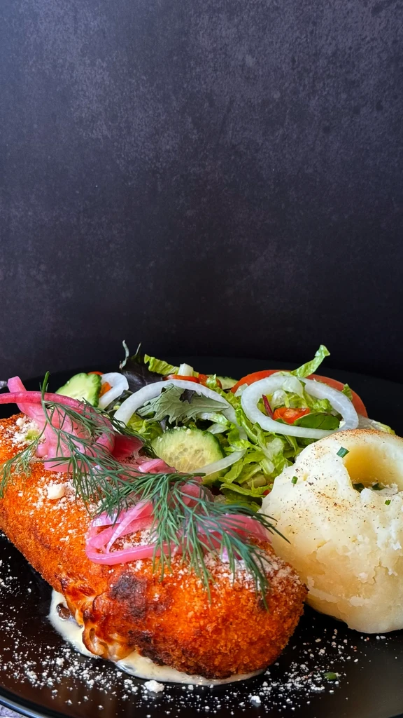 Plated breaded entree, mashed potatoes, green salad, pickled onions, and dill.