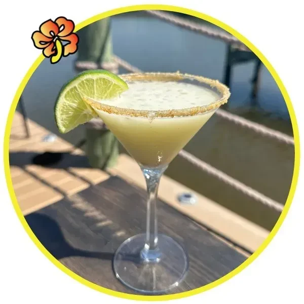 Frothy greenish cocktail with lime, spiced rim, on a sunny dock.