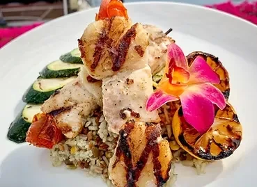 Grilled skewer with scallops and meat, grains, zucchini, orchid on white plate.