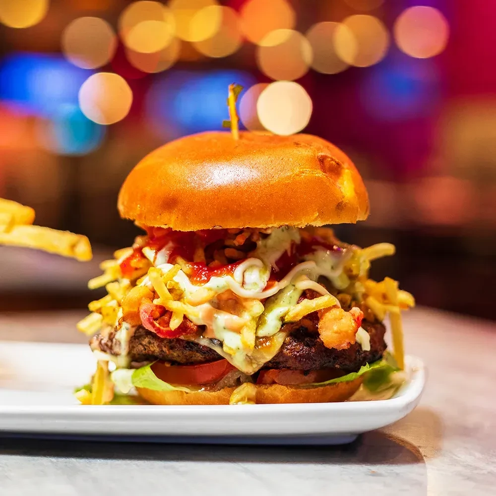 Detailed close-up of gourmet burger with fries and two sauces.