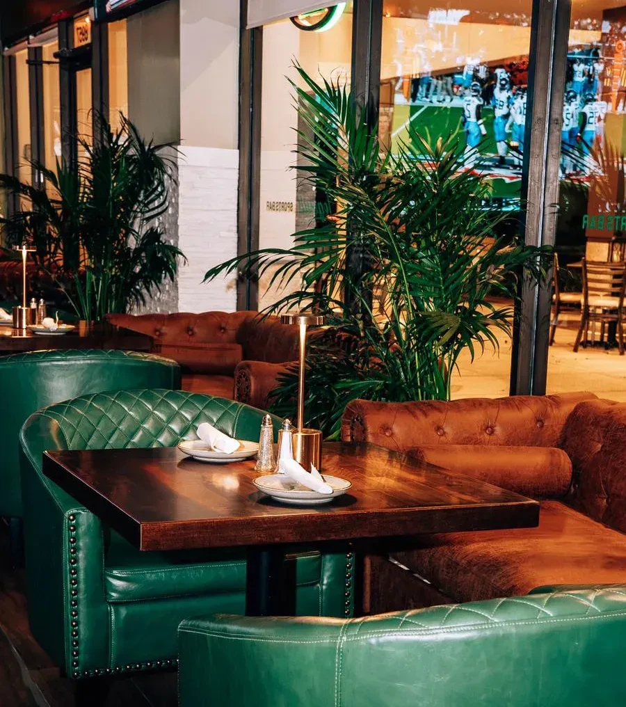 Stylish restaurant with emerald armchairs, brown banquettes, and set table.
