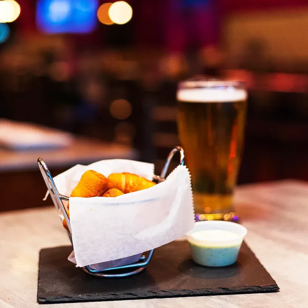 Close-up of fried pastries, dipping sauce, and beer in a restaurant.