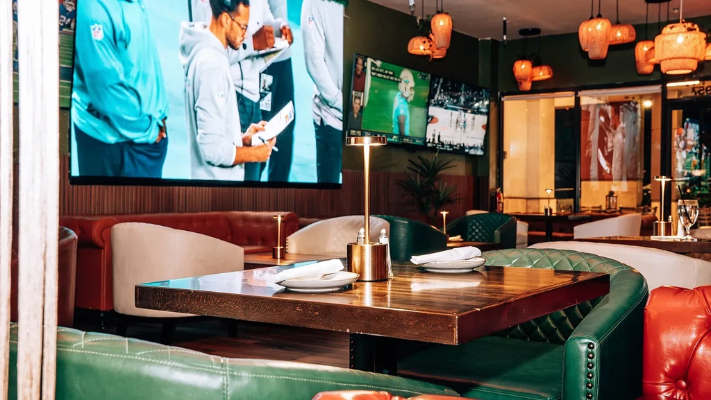 Modern sports bar with plush seating, set tables, and TVs.