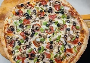 Overhead round pizza with pepperoni, mushrooms, olives, bell peppers on peel.