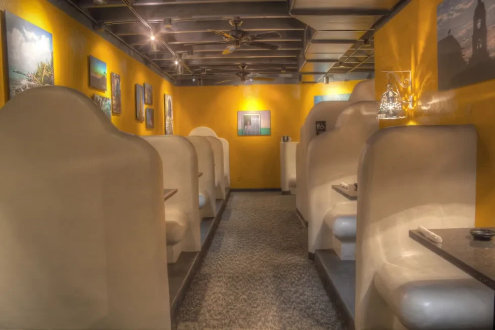 Restaurant dining area with vibrant yellow walls, art, industrial ceiling, and booths.