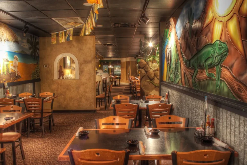 Colorful, empty restaurant interior with tropical-themed murals on walls.