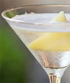 Close-up of clear martini cocktail with yellow triangular garnish.