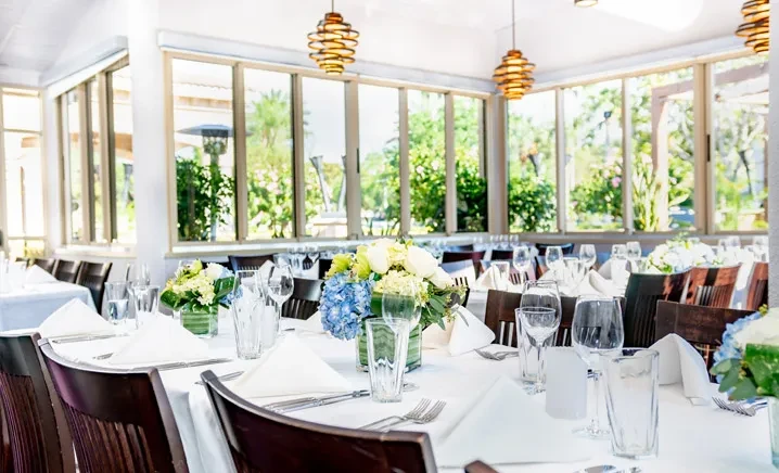 Elegant dining room, set tables, blue hydrangeas, garden view.