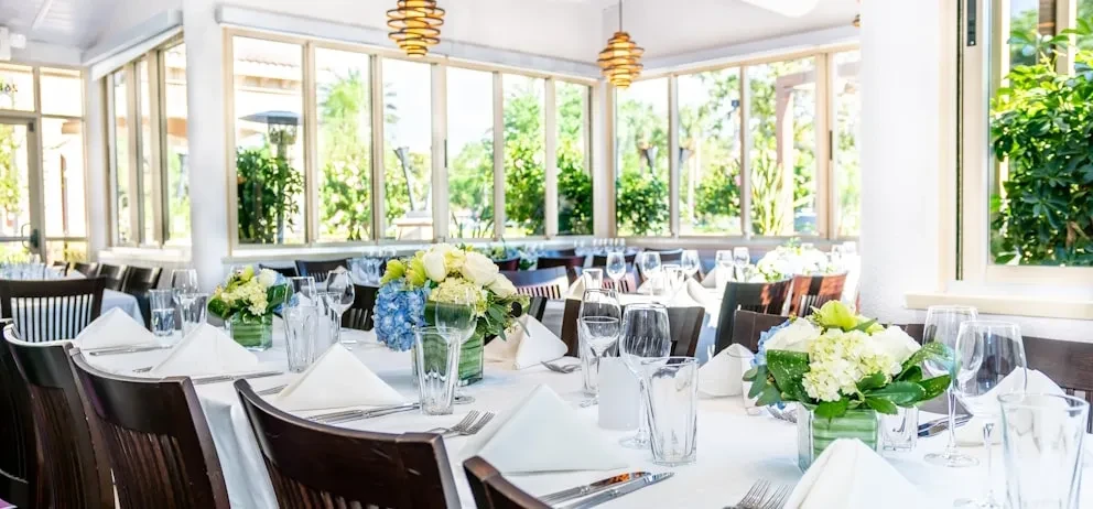 Elegant restaurant dining room with set tables, floral centerpieces, and large windows.