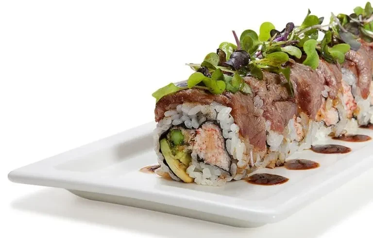 Close-up of a sushi roll topped with seared beef and microgreens.
