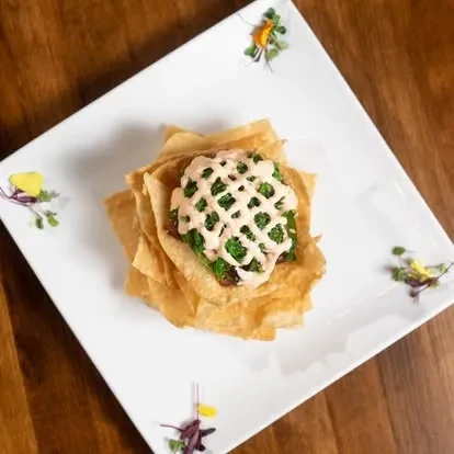 Appetizer: crispy wonton bowl, green filling, creamy sauce, microgreen garnish.
