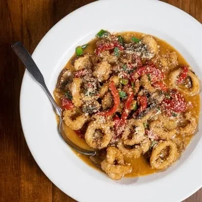 Fried calamari in reddish sauce, garnished with cheese, herbs, and bell pepper.