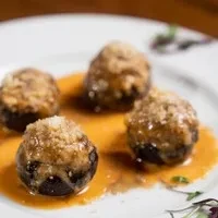 Four dark, breaded stuffed mushrooms or meatballs in savory sauce.