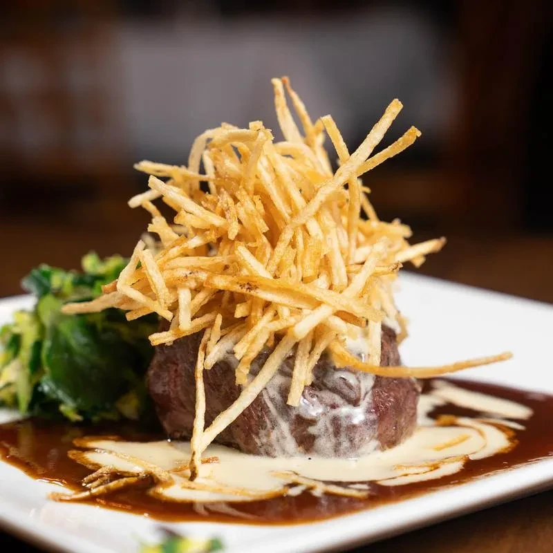 Plated medium-rare beef filet with shoestring fries, sauces, and vegetables.