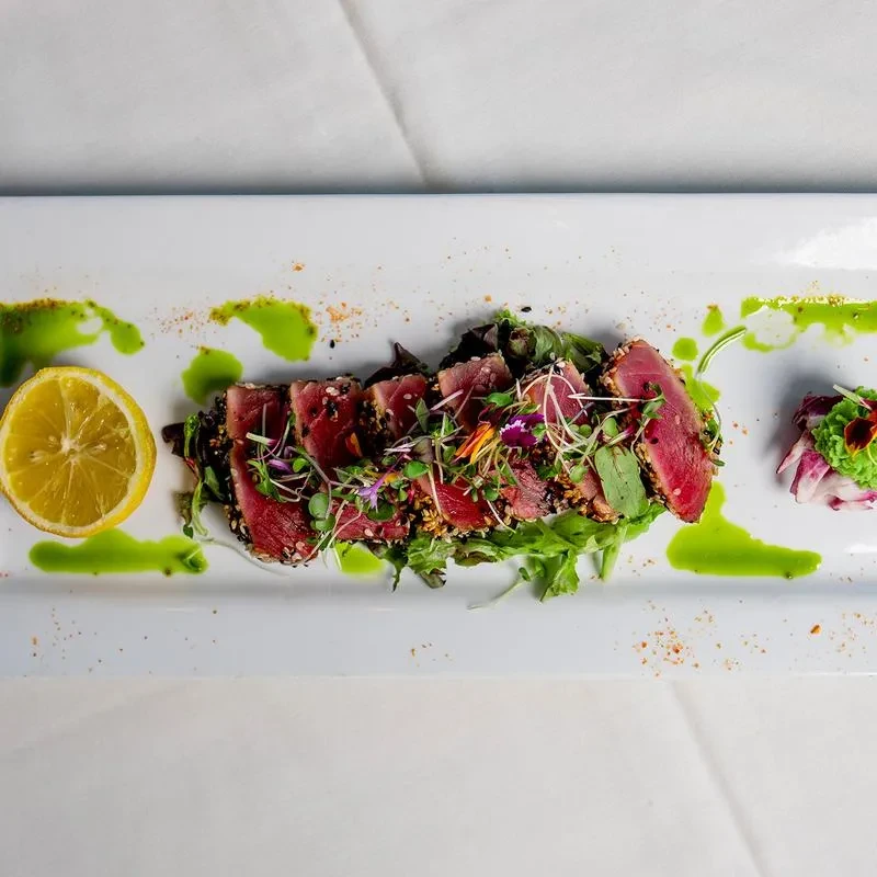 Seared tuna with sesame, greens, edible flowers, lemon, and sauce.