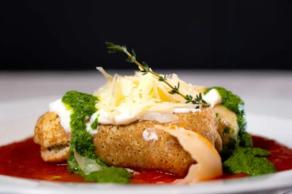 Two golden crepes with red sauce, cheese, cream, pesto, and thyme.