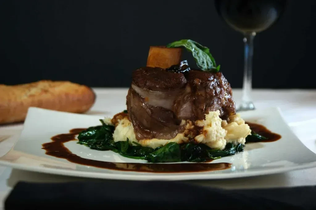 Plated braised short rib, mashed potatoes, greens, and dark sauce.