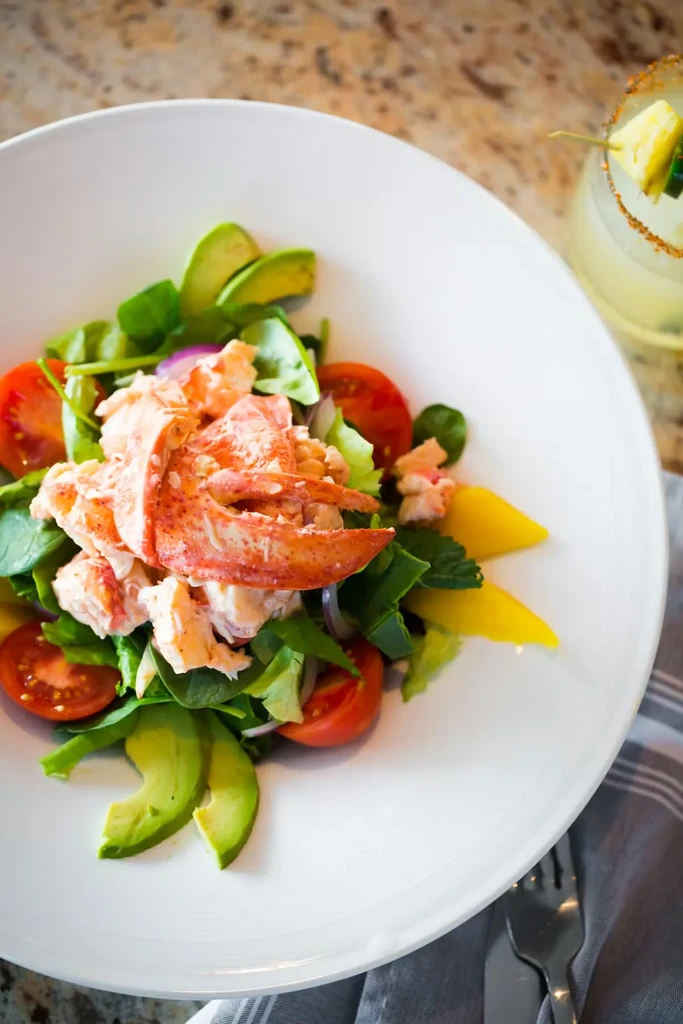 Lobster salad with greens, avocado, tomatoes, and a garnished beverage.
