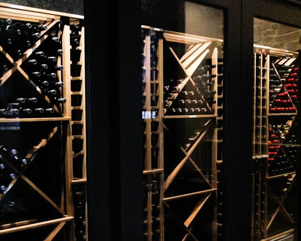 A well-stocked wine cellar with bottles in wooden racks behind glass.