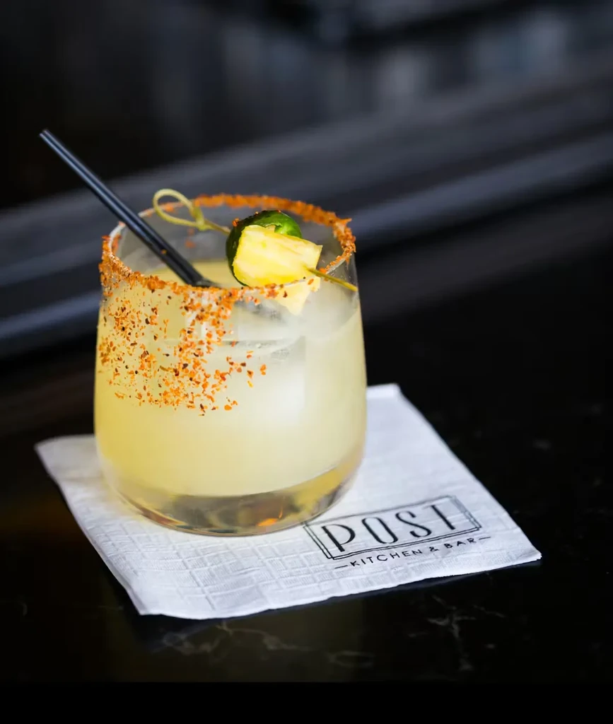 Chili-lime rimmed cocktail with pineapple, jalapeño, and POST KITCHEN & BAR logo.