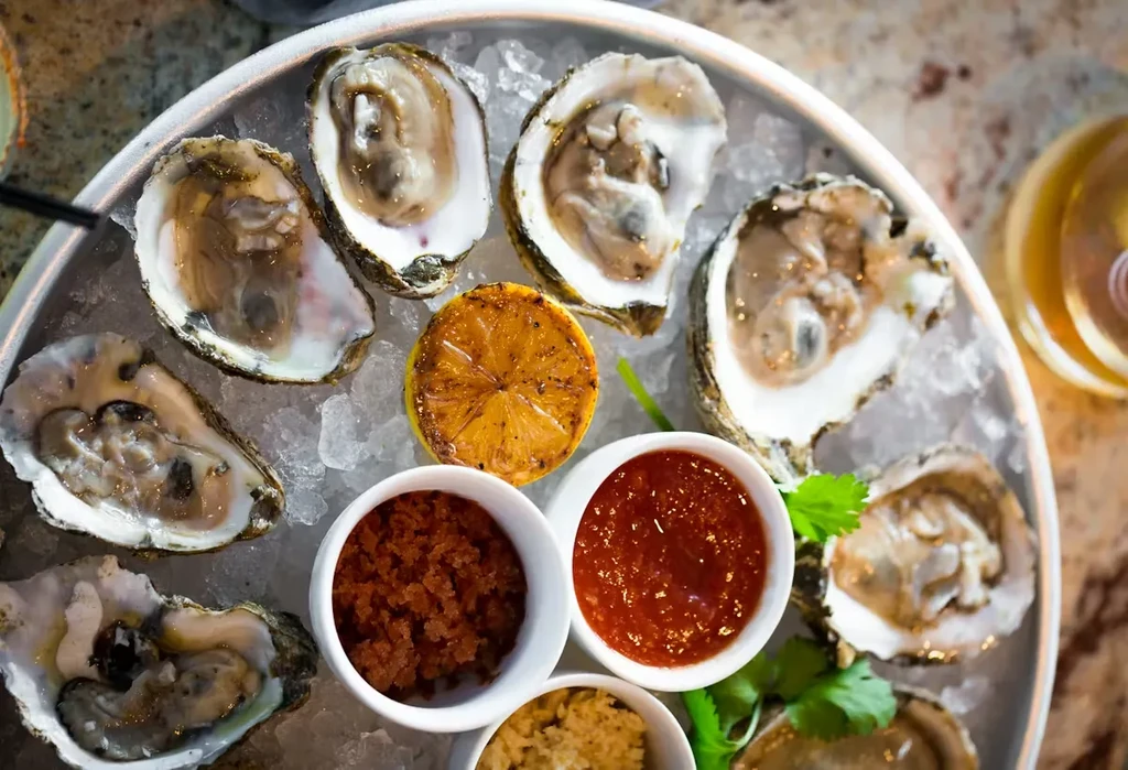 Close-up of shucked oysters on ice with lemon and condiments.