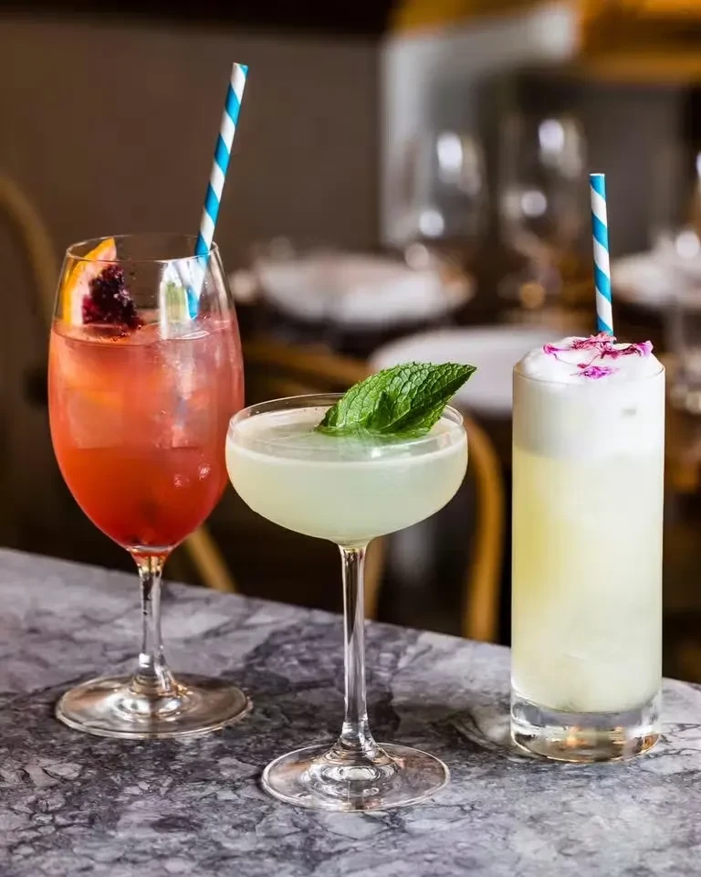 Three colorful cocktails in various glasses on a marbled counter.