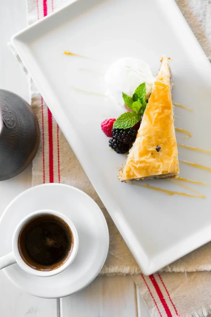 Golden baklava with berries, ice cream, and espresso on white wood.