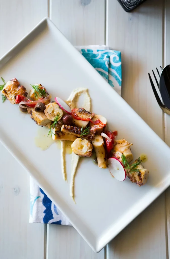 Grilled octopus, vegetables, and sauce on a white plate.