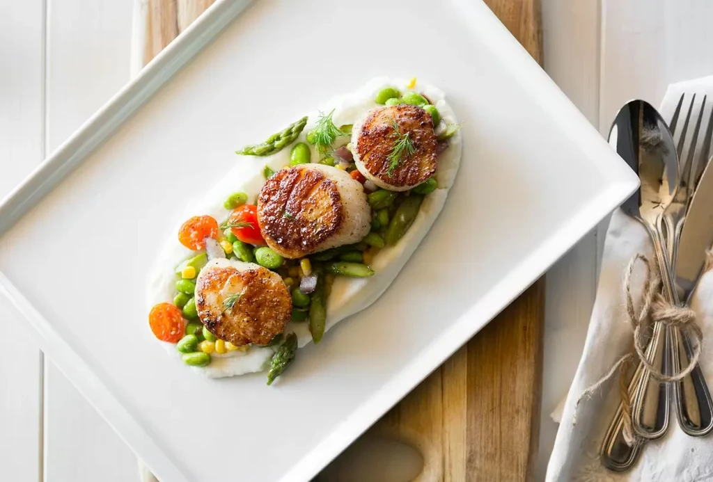 Pan-seared scallops with creamy puree, dill, and colorful mixed vegetables.