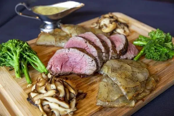 Medium-rare sliced beef platter with broccolini, mushrooms, and potatoes.