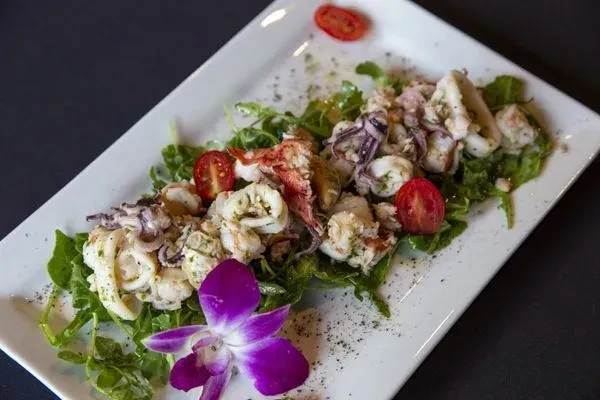 Plated seafood salad with greens, tomatoes, and a purple orchid.