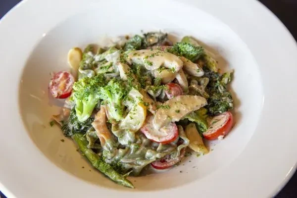 Creamy pasta dish with broccoli, tomatoes, and herbs in a white bowl.
