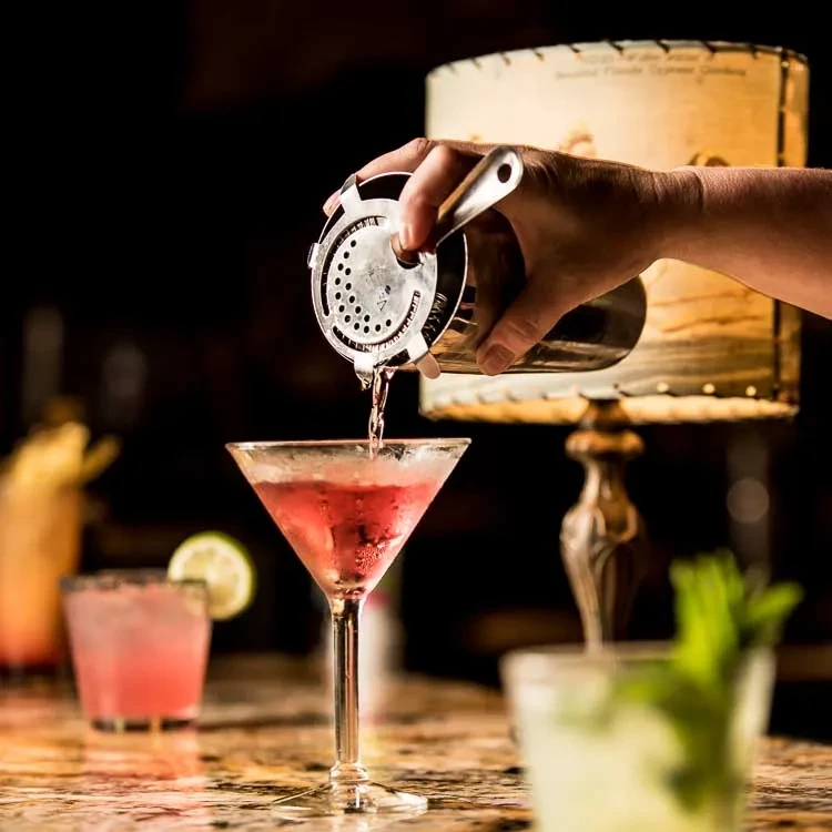 Hand pours pink cocktail from shaker into chilled martini glass.